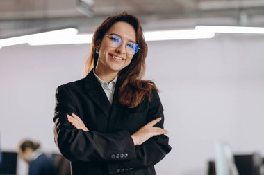 Ambitious businesswoman in glasses posing with folded hands. Confident female entrepreneur smiling on blurred background. Successful woman. High quality photo