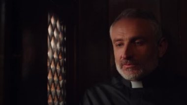 Catholic priest talking to parishioner in confessional booth. Pastor listening the confession in church. Clergyman giving advice to the churchgoer. High quality 4k footage