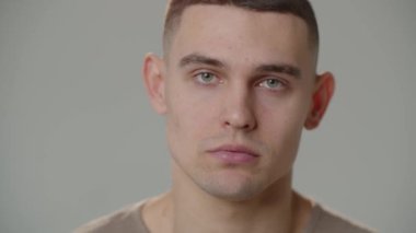 The young man raises his eyes and looks into the camera. Close-up of a young man with a close look against a white wall. High quality 4k footage