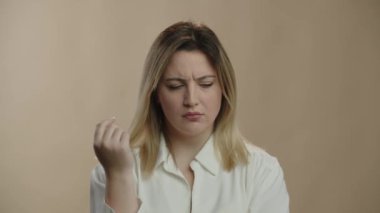 Blonde woman trying to remember something. Girl in white shirt frowning and shaking her head on brown background. High quality 4k footage