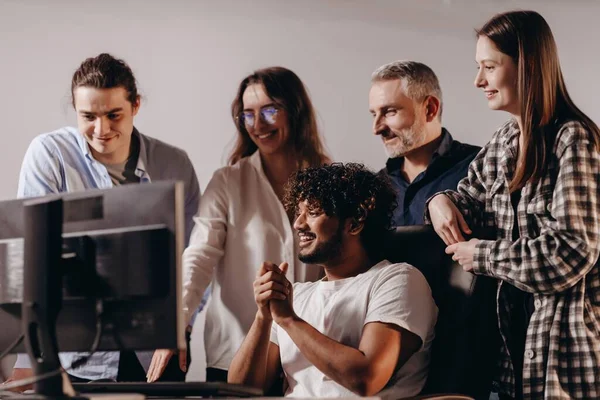 Diverse business team having fun during workday. Smiling coworkers looking at the monitor. Excited startup managers enjoying work results. High quality photo