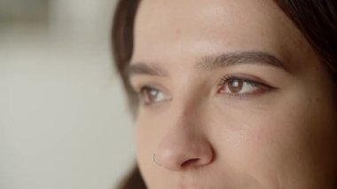 Cropped view of female face of brunette woman. A young woman with brown eyes and a nose piercing smiles and looks at the camera. High quality 4k footage
