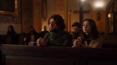 A married couple at a Sunday service. Husband and wife fold their hands in prayer while sitting in a catholic church. High quality 4k footage