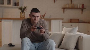 A man sitting on the couch is very concentrated playing a game console. A young man celebrates a victory after completing a very difficult level in a video game. High quality 4k footage