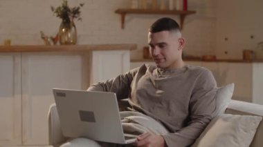 Genç serbest çalışan kanepede uzanıp gülerken dizüstü bilgisayardan komik videolar izliyor. Adam bilgisayarda komik videolar izleyerek kısa bir ara verdi. Yüksek kalite 4k görüntü