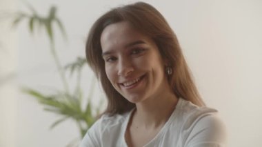 Sabahları gülümseyen cilveli kız. Güzel kahverengi gözlü esmer bir kadın tatlı bir gülümsemeyle kameraya bakıyor. Evdeki mutlu genç bayanın kapalı çekim görüntüleri. Yüksek kalite 4k görüntü