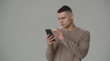 Akıllı telefonuyla haber kanallarını karıştıran düşünceli genç adam. Kısa saçlı, akıllı telefonunu kullanan bir adamın stüdyo fotoğrafı. Yüksek kalite 4k görüntü