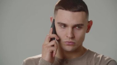 Ciddi bir adam telefonda bir şey tartışıyor ve başını sallıyor. Kısa saçlı bir adam beyaz arka planda dikilirken telefonla konuşuyor. Yüksek kalite 4k görüntü