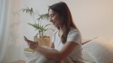 Sabahın köründe uyanan bir kadın cevapsız mesajlara cevap verir. Uzun saçlı, gülümseyen bir esmer elinde telefonla yatakta oturmuş bir şeyler yazıyor. Yüksek kalite 4k görüntü