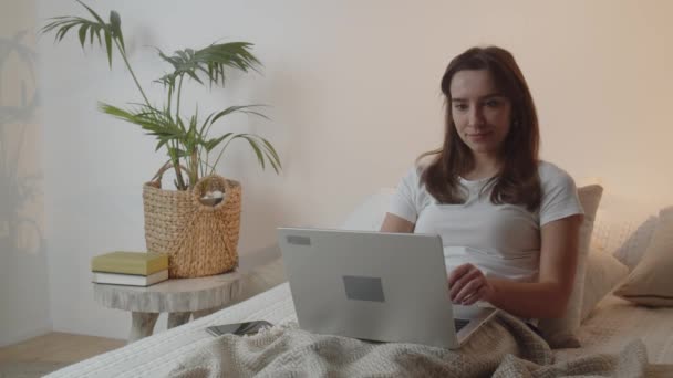 Morena Sorridente Está Trabalhando Seu Laptop Enquanto Está Deitada Cama — Vídeo de Stock