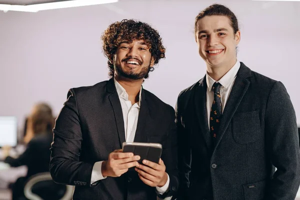 2人の若いビジネスマンがカメラで笑っている 黒いジャケットの幸せな起業家の屋内ショット ビジネスパートナーが一緒にポーズ 成功した人 高品質の写真 — ストック写真