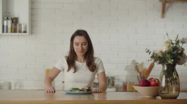 Diyet yapan genç bir kadın sebze salatası yiyor. Esmer bir kadın elinde bir tabak sebze salatası ve çatalla masaya oturur. Yüksek kalite 4k görüntü