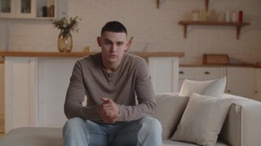 Endişeli bir adam kanepede otururken başını tutar. Kısa saçlı adam kötü haber beklentisiyle başını tutar ve iç çeker. Yüksek kalite 4k görüntü