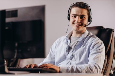 Mavi gömlekli, gülümseyen çağrı merkezi operatörü. Teleskop pazarlamacısı olarak çalışan mutlu genç bir adam. Müşteri destek ajansının kapalı çekimleri. Yüksek kalite fotoğraf