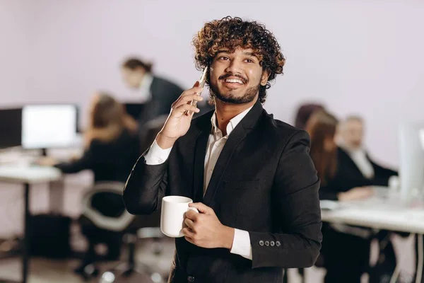 興奮した若いビジネスマンが電話で話している コーヒーを飲みながら笑顔のオフィスワーカーの屋内ショット 正式な服装でオフィスマネージャー 高品質の写真 — ストック写真