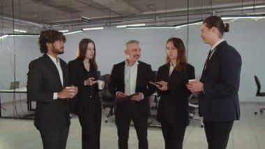 Bir grup deneyimli girişimci ofiste dikilip bir şeyler konuşuyorlar. Takım elbiseli insanlar öğle yemeği aralarında sohbet edip kahve içiyorlar. Yüksek kalite 4k görüntü