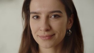 Uzun saçlı esmer, kameraya bakar ve gülümsemeye başlar. Burnunu beyaz bir duvara delip geçen gülümseyen bir esmer. Yüksek kalite 4k görüntü