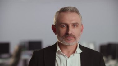 İş adamı kılığındaki orta yaşlı bir iş adamı kameraya bakar. Bulanık ofis arkaplanı önünde ciddi bir iş adamının portresi. Yüksek kalite 4k görüntü
