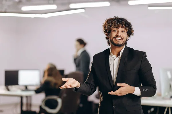 興奮したビジネスマンが何かを示す オフィスでのブラックスーツのジェスチャーで起業家を笑顔 ぼやけた背景で成功したマネージャー 高品質の写真 — ストック写真