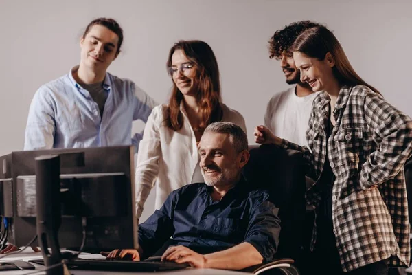 A senior employee of an IT company shows something on a monitor to his colleagues. An experienced worker shows the intricacies of work to new employees. High quality photo