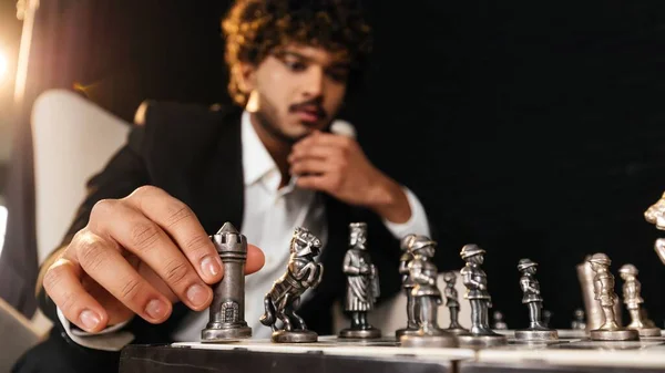 The chess player holds his hand to his chin and looks at the chessboard. Selective focus of businessman playing chess. Pensive entrepreneur thinking about business strategy. High quality photo