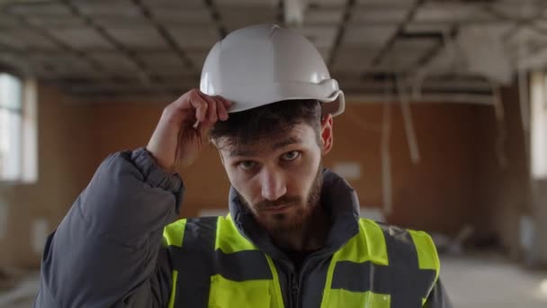 男性のビルダーは 彼の頭の上に白い保護ヘルメットを調整します 工事現場でのハードハットの建築家の正面図 高品質4K映像 — ストック動画