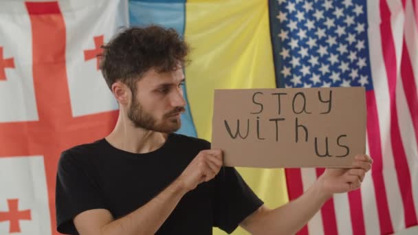站在格鲁吉亚 乌克兰和美国国旗旁边的年轻人 一名男性示威者展示了一个立场与我们的标语牌 政治行动 高质量的4K镜头 — 图库视频影像