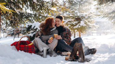 Evli bir çift karlı bir ormanda piknik yaptı. Genç insanlar küçük bir ateşin önünde oturup krep yerler. Yüksek kalite fotoğraf