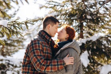 Karlı bir ormanın ortasında genç evli bir çiftin yakın çekimi. Bir kış ormanının arka planında duran genç insanlar birbirlerine sarılıyorlar. Yüksek kalite fotoğraf