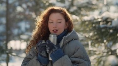 Tatlı kızıl saçlı kadın kış parkında sabah yürüyüşü sırasında termostan çay içer. Uzun bir yürüyüşten sonra donan kız ısınmak için sıcak çay içer. Yüksek kalite 4k görüntü