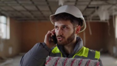 İnşaat alanında beyaz kasklı bir adam telefonda konuşuyordu. Boya silindirli müteahhit telefonla yapılan işi ustabaşına bildiriyor. Yüksek kalite 4k görüntü