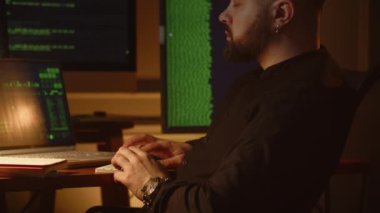 Ofiste dizüstü bilgisayarla çalışan bir bilişim şirketinin genç çalışanının görüntüsü. Genç bir programcı, kod satırları çalışan monitörlerin önünde oturur ve yazılım testleriyle meşgul olur. Yüksek kalite 4k