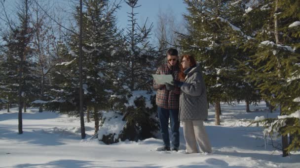 在一个阳光明媚的冬日 一对已婚夫妇在森林里散步 两个年轻人手拿着地图站在白雪覆盖的森林中间 讨论着什么 高质量4K — 图库视频影像