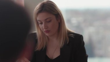 Takım elbiseli genç bir sarışının yakın çekimi. Belgeleri dikkatle inceliyor. Finans şirketinde çalışan sarışın bir kadın, mali raporların doğruluğunu kontrol ediyor.