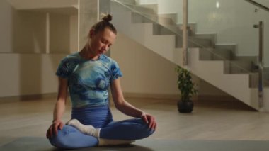 Lotus pozisyonunda oturan bir kadın boyun kaslarını ısıtmak için başıyla dairesel hareketler yapar. Genç bir kadın yoga minderinde otururken esneme egzersizleri yapıyor. Yüksek kalite 4k görüntü