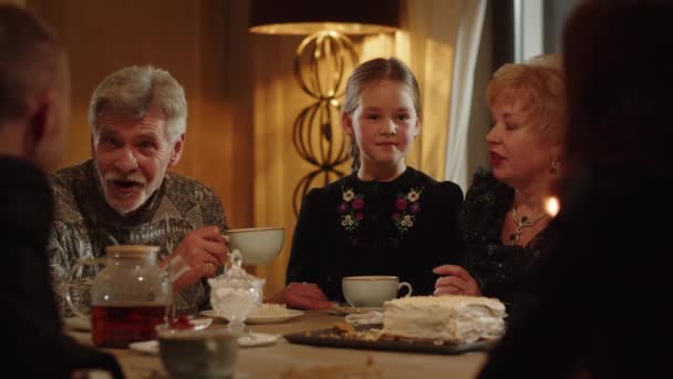 幸せな白人の家族はケーキを食べ テーブルでお茶を飲み 何かについてかわいい会話をしています 笑顔の高齢者の近くのテーブルに座って 彼らの話を — ストック動画