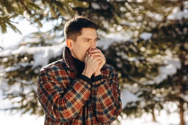 ブルネットの男は冬の公園で手を暖める 寒い日に雪の森にポーズをとるジャケット姿の青年の屋外撮影 高品質の写真 — ストック写真