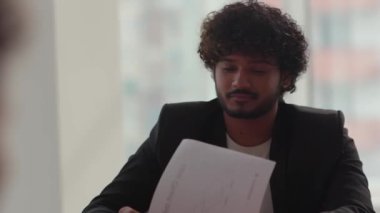 Siyah takım elbiseli genç bir adamın yakın çekimi. Belgeler üzerinde çalışıyor. Hintli bir işadamı toplantı sırasında şirketlerin mali beyanlarını inceliyor. Yüksek kalite 4k görüntü