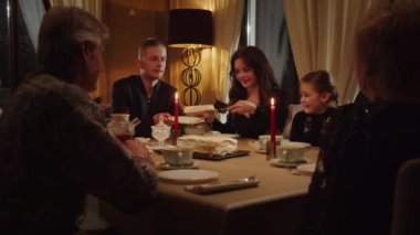 Bir grup insan akşam yemeğinden sonra bir restoranda oturup çay içiyor ve tatlı yiyorlar. Genç bir kadın bir parça kek keser ve kocasının tabağına koyar. Dost bir aile akşam yemeği yiyor.