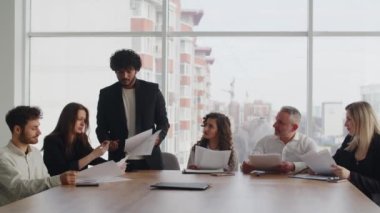 Toplantıda genç bir Hintli işadamı, ortaklarına şirketlerin yeni finansal modelinin faydalarını anlatıyor. İş kıyafetleri içinde bir grup insan raporları gözden geçirir ve optimize etmenin yollarını tartışır.