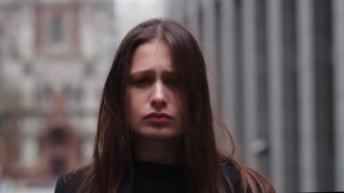 Neredeyse sokakta ağlayan üzgün genç bir kadının portresi. Üzgün kız kameraya bakıyor. Bulanık şehir geçmişinde depresyondaki esmer kız. Yüksek kalite 4k görüntü