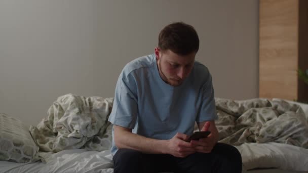 Ung Man Blå Shirt Använder Smartphone När Han Sitter Sängen — Stockvideo