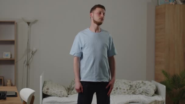 部屋の真ん中に立っている男は首と肩を暖めるための演習を実行します 若い男が朝食前に朝のワークアウトを行う 健康的なライフスタイルのコンセプト 高品質4K — ストック動画