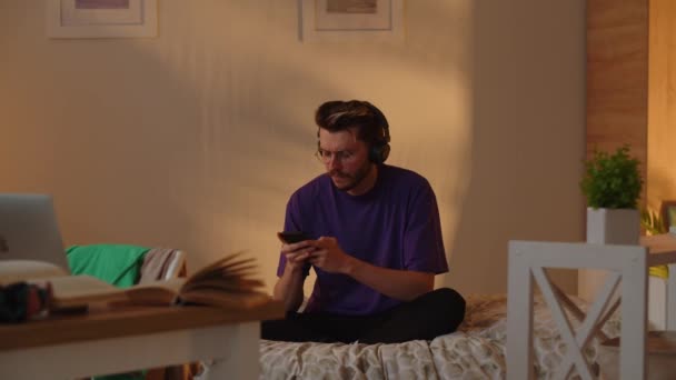 Homem Com Uma Camiseta Roxa Senta Cama Ouve Sua Música — Vídeo de Stock