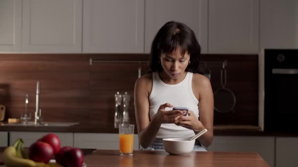 Woman Sits Table White Bowl Glass Orange Juice Watches Something — Stock Video