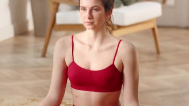Genç kadın evde yoga yapıyor ve derin nefes veriyor. Sportif kız oturma odasında meditasyon yapıyor. Yüksek kaliteli FullHD görüntüler