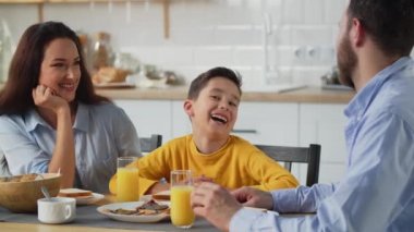 Mutlu aile birlikte kahvaltı yapar. Ebeveynler ve oğulları kahvaltıda meyve suyu ve tost yer. Yüksek kalite 4k görüntü