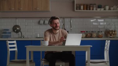 Elinde bir fincan kahve ve dizüstü bilgisayarla masada oturan gülümseyen adam video aracılığıyla biriyle iletişim kuruyor. Evden çalışan bir erkek serbest yazar, yeni bir iş projesinin detaylarını kendi projesiyle tartışıyor.