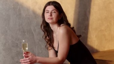 Siyah gece elbisesi giymiş genç bir bayan bir bardak şarapla oturur ve kameraya gülümser. Elbise giymiş güzel bir esmer merdivenlerde oturur ve bardaktan beyaz şarap içer. Yüksek kalite FullHD