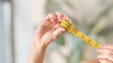 Kadın eli sarı bir mezura çıkarır. Bir kadın bir santimetre bant ile ölçü alır. Yüksek kaliteli FullHD görüntüler